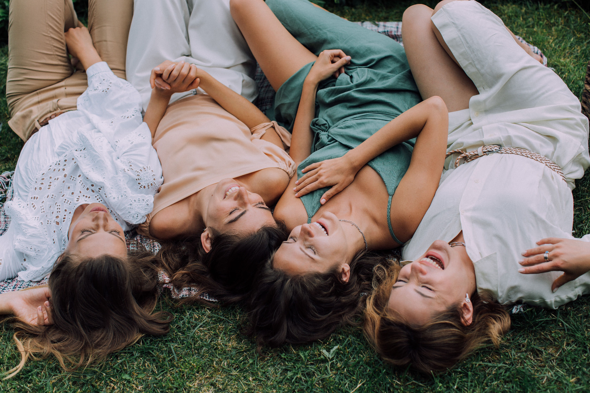 four women laughing together lying on grass